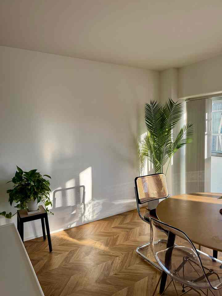 自然光が差し込むナチュラルな色調のダイニングスペース、木製のダイニングテーブルと透明およびラタンの椅子が配置され、温かみのある雰囲気を醸し出している。