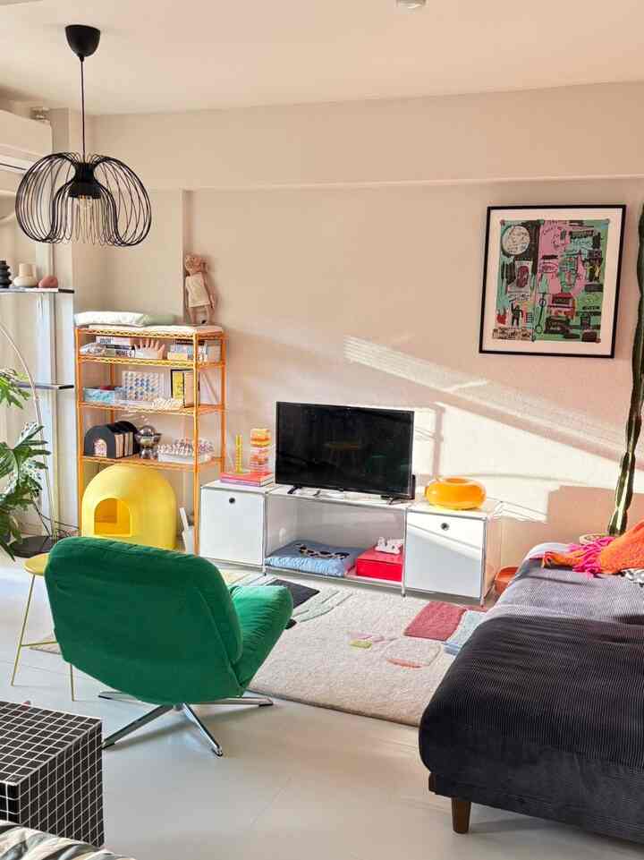 黒と黄色のトーンのリビングルーム、緑のアームチェアと大きなソファ、カラフルなポスターとペンダントライトが置かれた印象的な空間