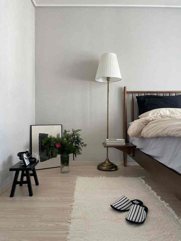 A modern bedroom with white walls and wood-tone bed frame, featuring beige bedding and a floor lamp creating a cozy atmosphere