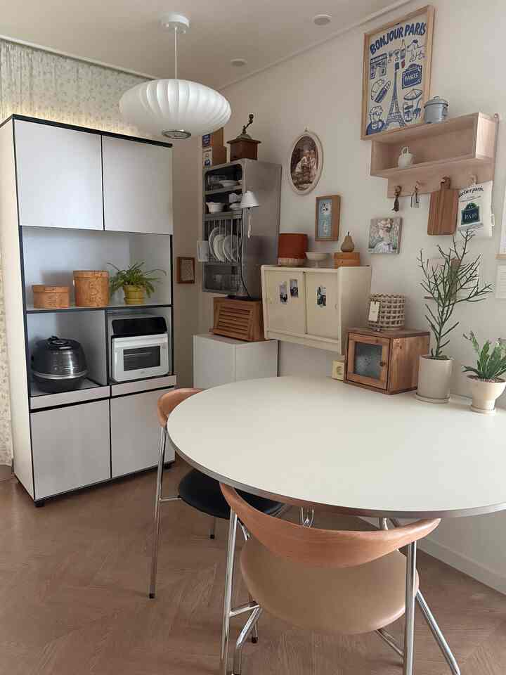 白と茶色のトーンでまとめられたキッチン、木製のダイニングチェアとキャビネット、ペンダントライトが配置された雰囲気のあるインテリア