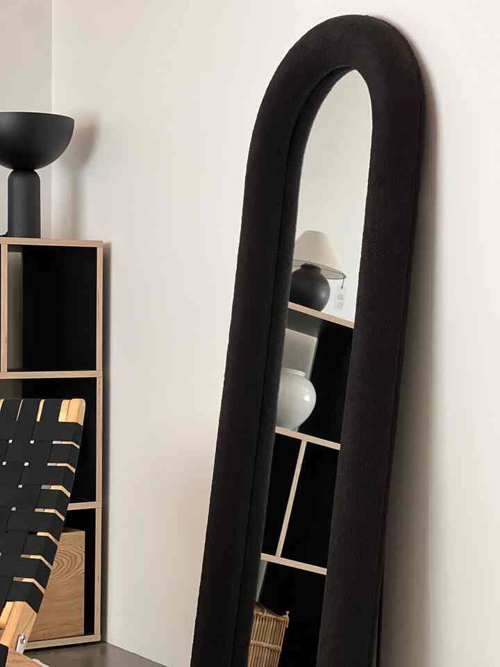 ブラックとウッドトーンが調和したモダンな玄関空間、大きな黒い鏡とオープンシェルフ、アームチェアが配置されている