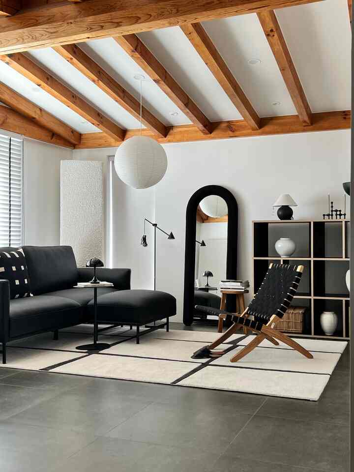Modern living room with white walls and wood-tone ceiling beams, featuring black sofa and lounge chair in a clean setting