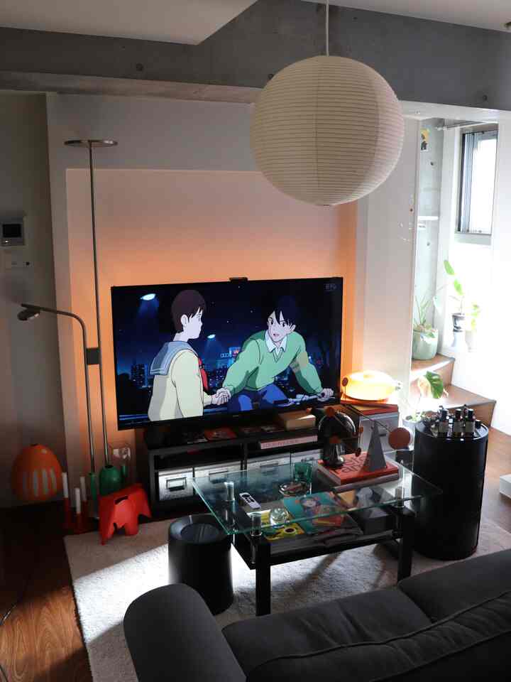 ブラウンの木製床と黄色のバックライト壁が調和したミッドセンチュリーモダンのリビング、グレーのリクライニングソファとガラスのコーヒーテーブルが配置された印象的な空間