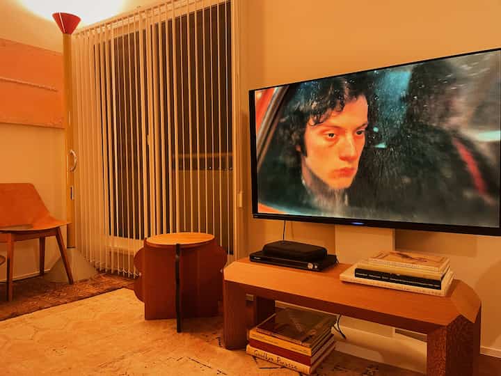 暖かいオレンジ色調のリビング、ミッドセンチュリーモダン家具とテレビ台、フロアランプが印象的な空間を演出する。