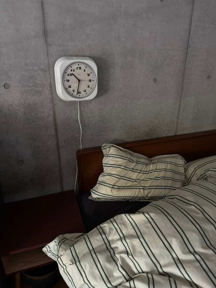 Mid-century modern bedroom with gray concrete wall, brown wooden bed frame, and striped duvet cover