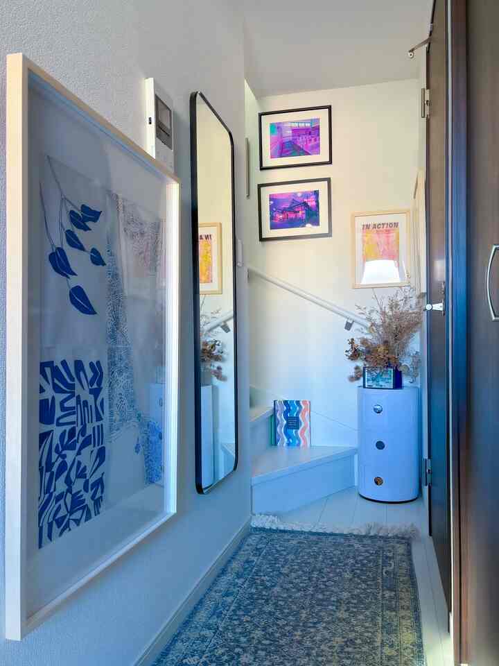 Bright white corridor with blue rug featuring picture frames and a tall mirror, creating an artistic atmosphere