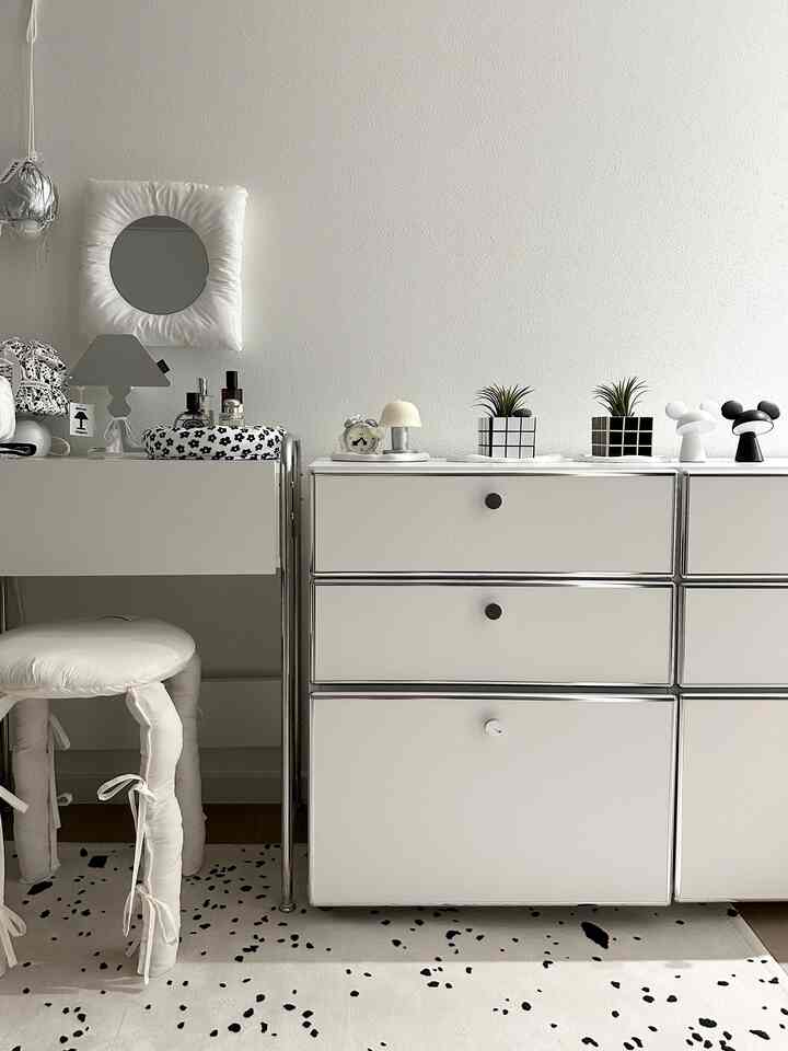 A simple room in white and black tones featuring mini plants, a vanity, and a cushioned stool in a monotone interior