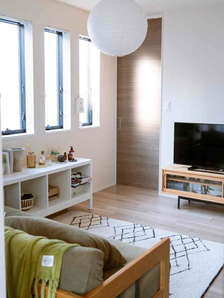 白い壁と木目調の床が調和したコンパクトなリビング、低めのソファとテレビ台が配置されたすっきりとした空間