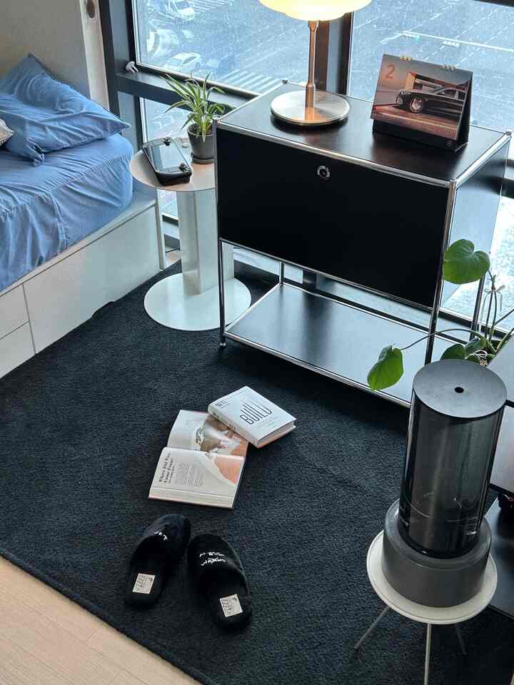 モノトーンブラックを基調とした寝室インテリア、ブラックラグとキャビネット、ブルーベッドとサイドテーブルが配置された洗練された空間