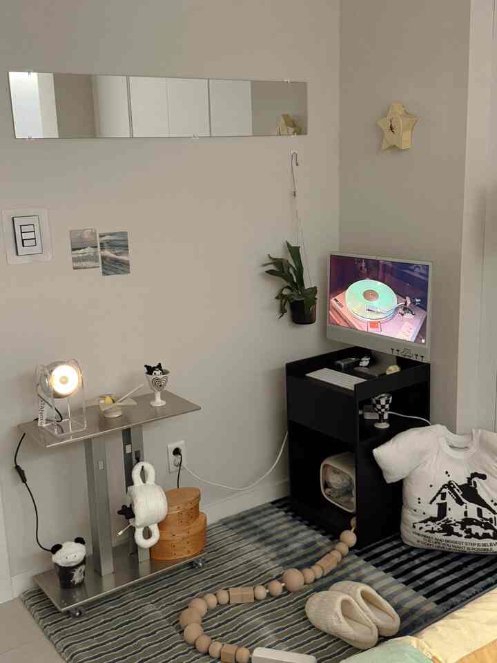 ナチュラルトーンのコンパクトな部屋、黒いデスクとメタルのサイドテーブル、ブルーストライプのラグが配置されたシンプルで北欧風のインテリア