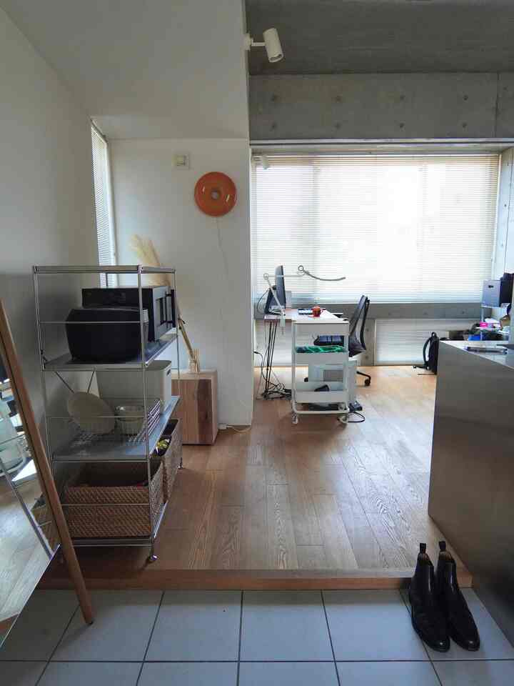 白い壁と木目調の床、デスクとオフィスチェアが配置された一人暮らしのワンルーム、明るくコンパクトな空間