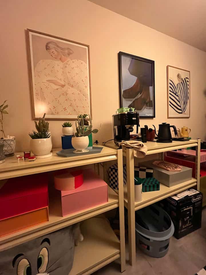 ベージュの壁とスチール製5段収納ラックが置かれたキッチンワゴンの空間、アートポスターとホームカフェ要素が調和した温かみのあるインテリア