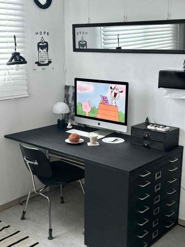 モノトーンのホームオフィス空間、黒いデスクと椅子、白い壁とブラインド、デスクには照明とコンピュータが配置された印象的なインテリア