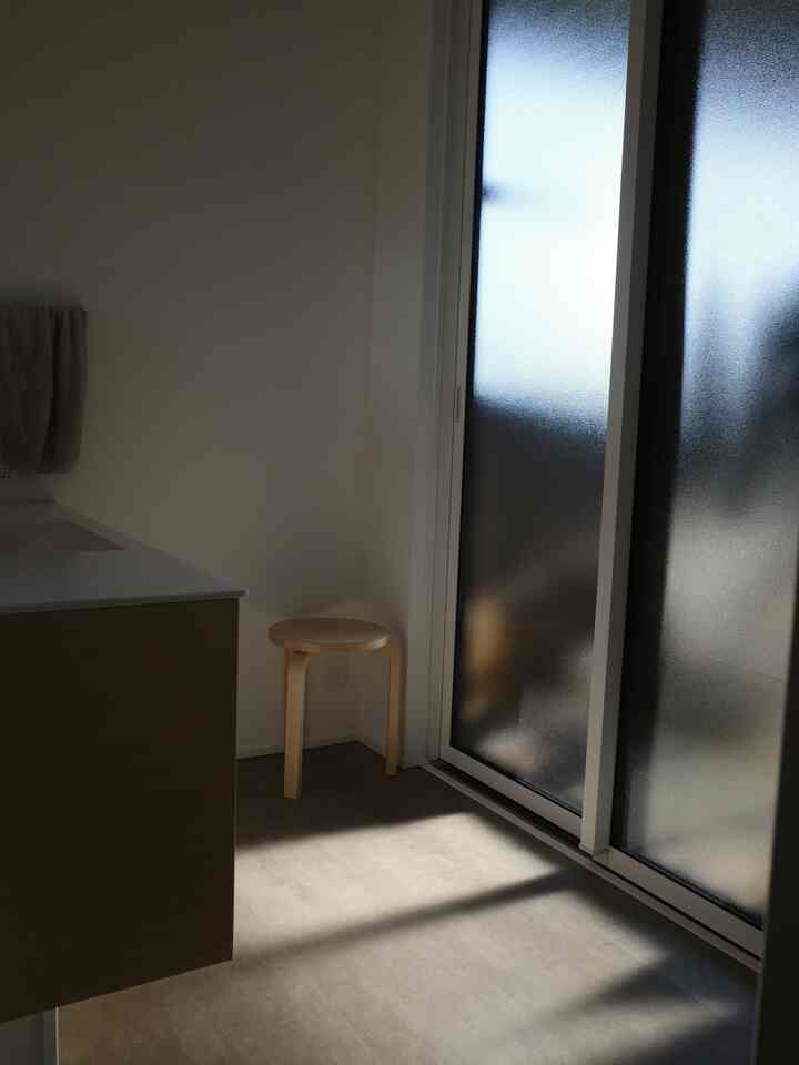 白い壁と木目調のスツールが配置された、バルコニーに繋がる明るい浴室空間