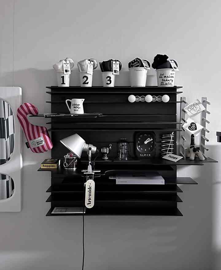 モノトーンの壁に黒い棚が配置され、多様なオブジェと照明があるモダンで洗練された壁飾りの空間