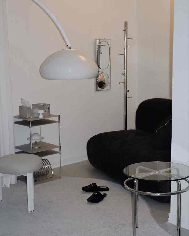 Modern living room with white walls and ceiling, featuring a black sofa, glass side table, round rug, and floor lamp in a minimalistic setting