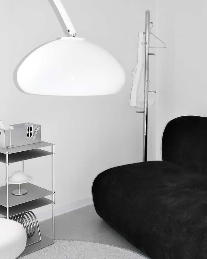Monotone living room with a black sofa, white pendant light, and metal storage shelves creating a simple interior