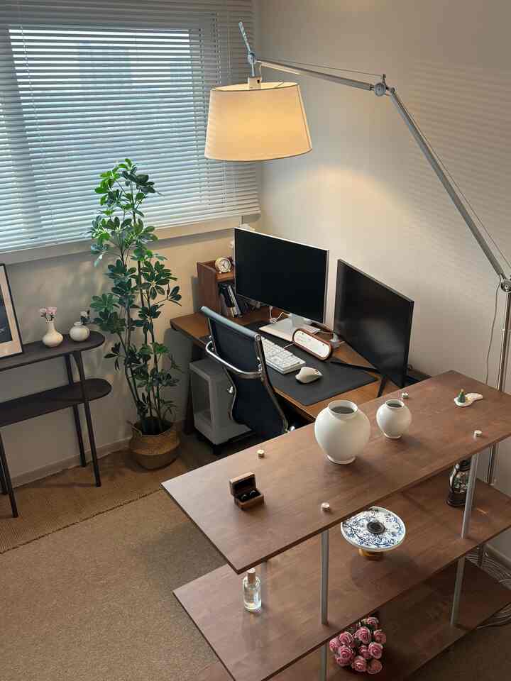 ホワイトとブラウンの色調の書斎、デュアルモニターのデスクとオフィスチェア、棚と植物が配置されたモダンで落ち着いたインテリア