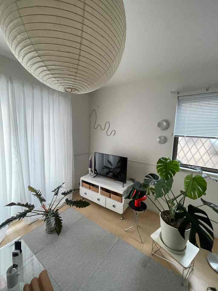 白と緑のトーンが印象的なリビング、ミッドセンチュリーモダンのペンダントライトと植物が配置された落ち着いた空間