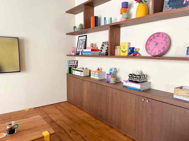 白い壁にブラウンの木製棚とキャビネットが配置されたリビング、カラフルな装飾品と時計が印象的な雰囲気のある空間