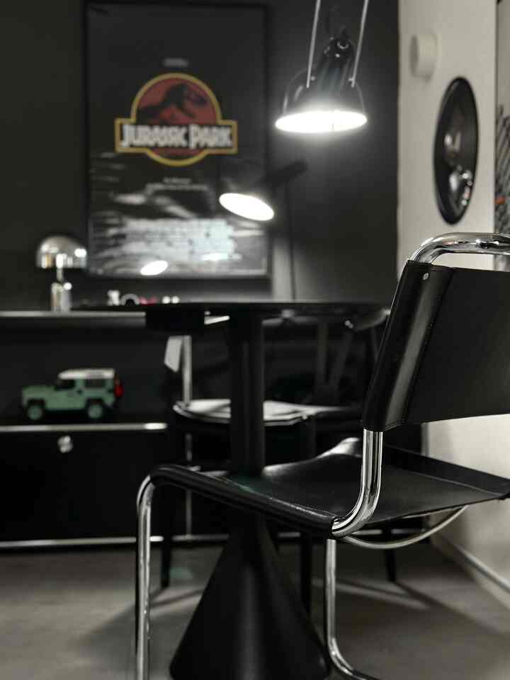 ブラックトーンのモダンダイニングルーム、クロームフレームのアームチェアと丸テーブルが配置された洗練された空間