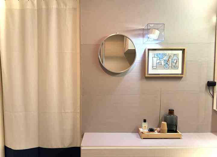 ナチュラルなベージュと木目調のパウダールーム、丸い鏡と壁の照明、きれいに配置された木製トレイが印象的なインテリア