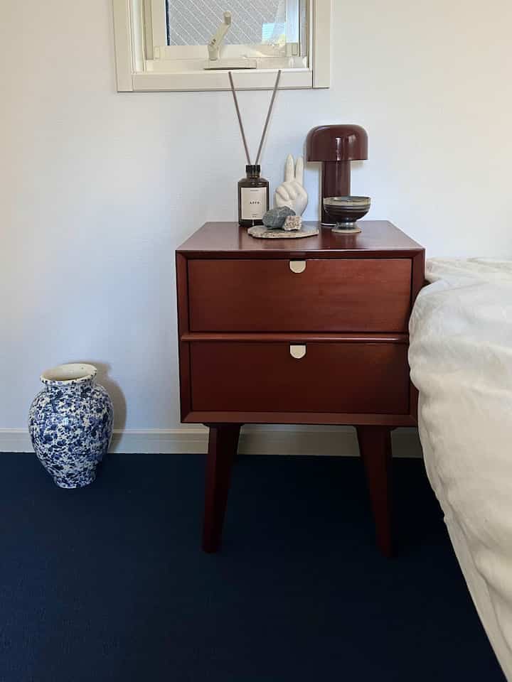Simple bedroom featuring navy carpet and brown side table with white bed bedding visible