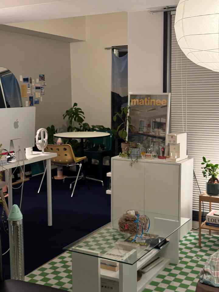 白とベージュのトーンのワンルーム、机とコーヒーテーブル、植物が配置されたモダンな在宅勤務空間