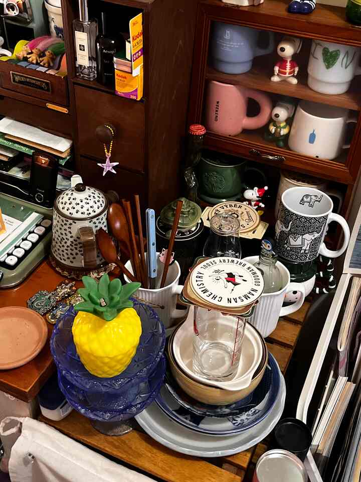 温かみのある木目調の狭く散らかった空間に、さまざまなボウルとマグカップが配置された印象的なインテリア