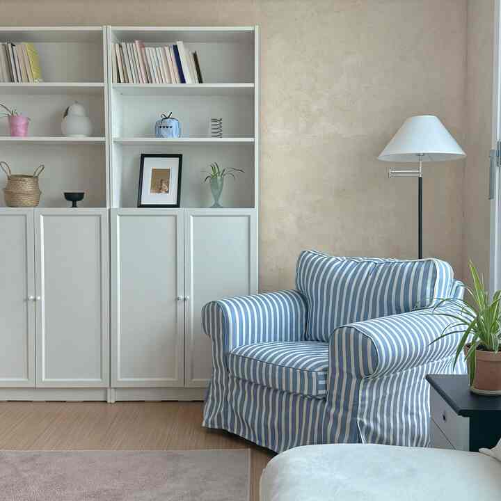 白とベージュの色調のリビング、本棚と青のストライプ柄アームチェアが置かれたシンプルでナチュラルな雰囲気のインテリア