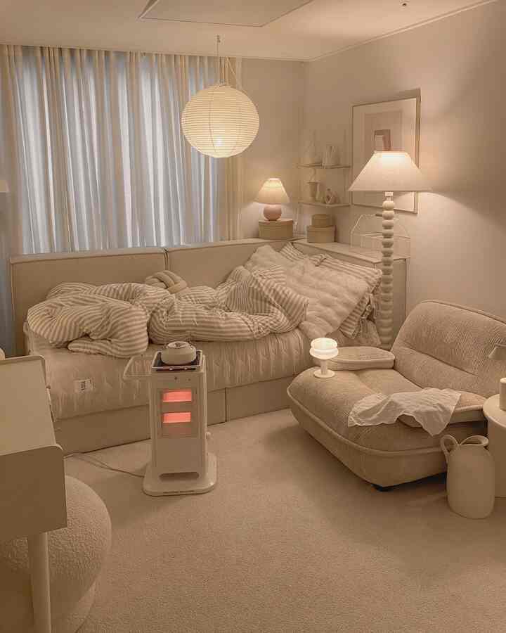 柔らかなベージュ色調の寝室、ストライプ柄の掛け布団、シングルソファ、暖かい照明と暖炉がある雰囲気のあるインテリア