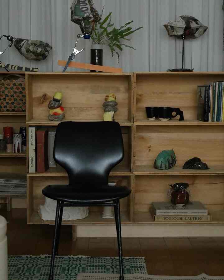 Natural and simple space featuring a brown wooden bookshelf and a black armchair, accented with plants and objets
