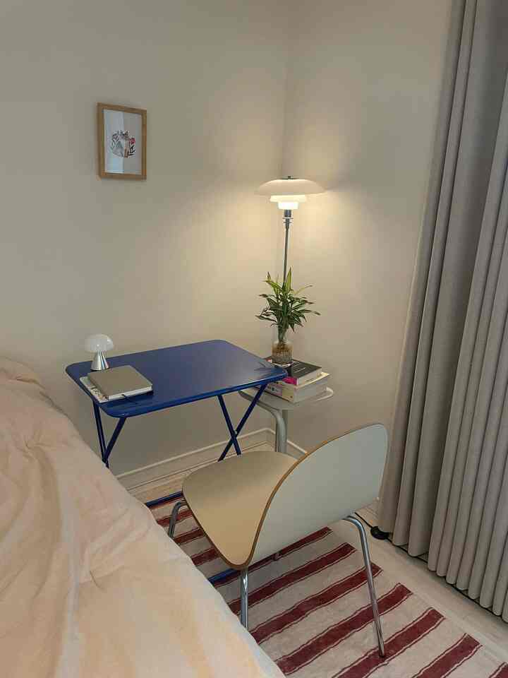 Beige and blue toned bedroom-side home office space featuring a blue table, beige chair, side table, and striped rug with cozy atmosphere