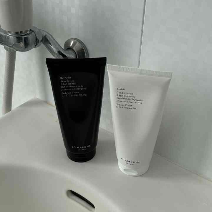 白いタイルの浴室に、清潔感のある洗面台とジョーマローンのバス用品が配置されたシンプルな空間