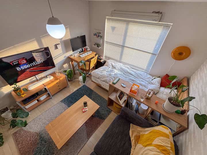 Natural wood-toned 1K studio apartment featuring bed, desk, and sofa arranged in a cozy single living space