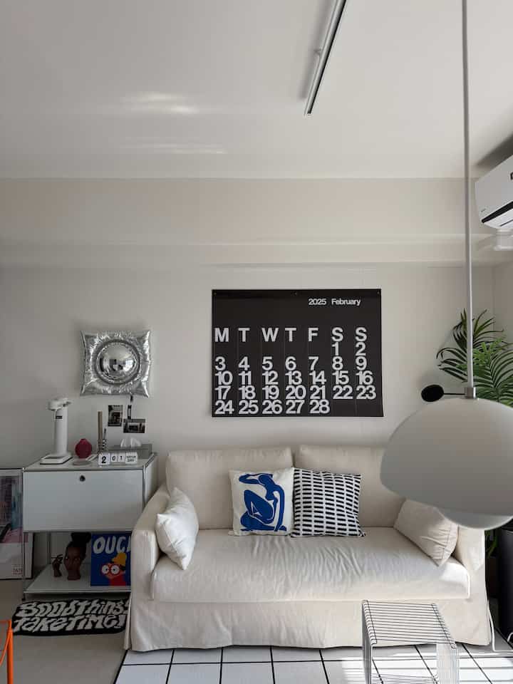 白とアイボリーの色調のリビング、シンプルなソファとパターンクッション、モダンなペンダントライトが配置されたミッドセンチュリーモダンスタイルの空間