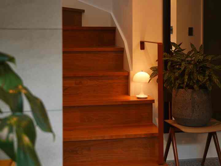 温かみのある木目調の階段と白いテーブルランプ、植物が配置された落ち着いた玄関スペース