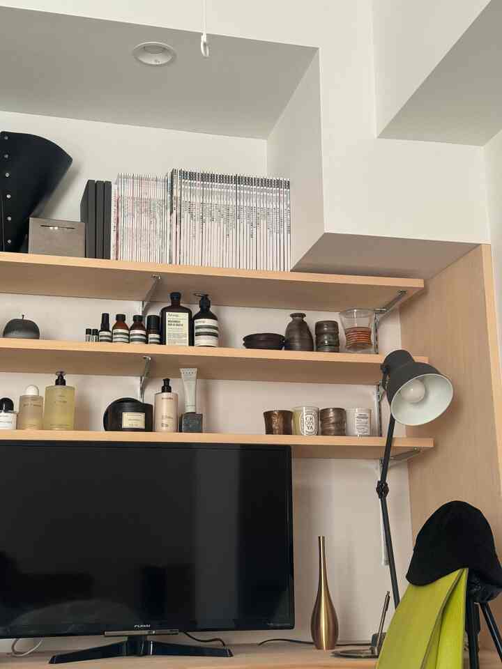 白い壁と木目調の棚が配置された一人暮らしの作業スペース、本やキャンドル、照明で雰囲気のあるインテリア