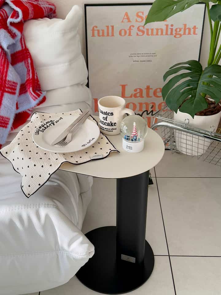 白と黒のトーンのカフェ風の室内、小さな丸テーブルに皿、マグカップ、スノードームと観葉植物が配置された印象的な空間