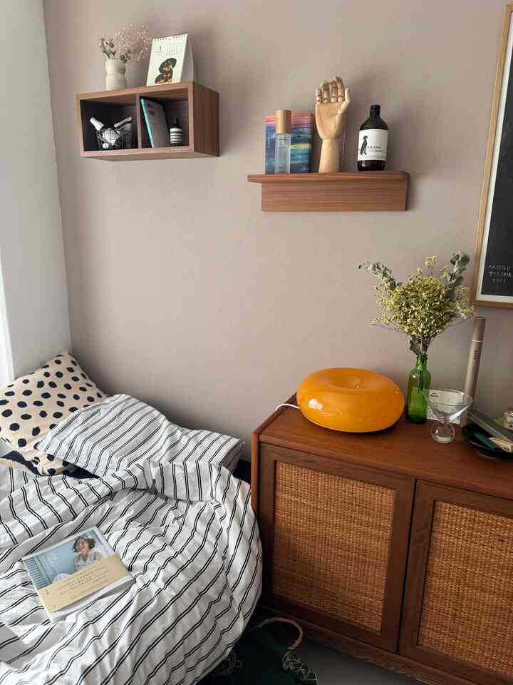 ベージュ色の壁と木製家具が調和する寝室、ストライプの寝具とクッション、本が置かれた落ち着いた雰囲気の空間