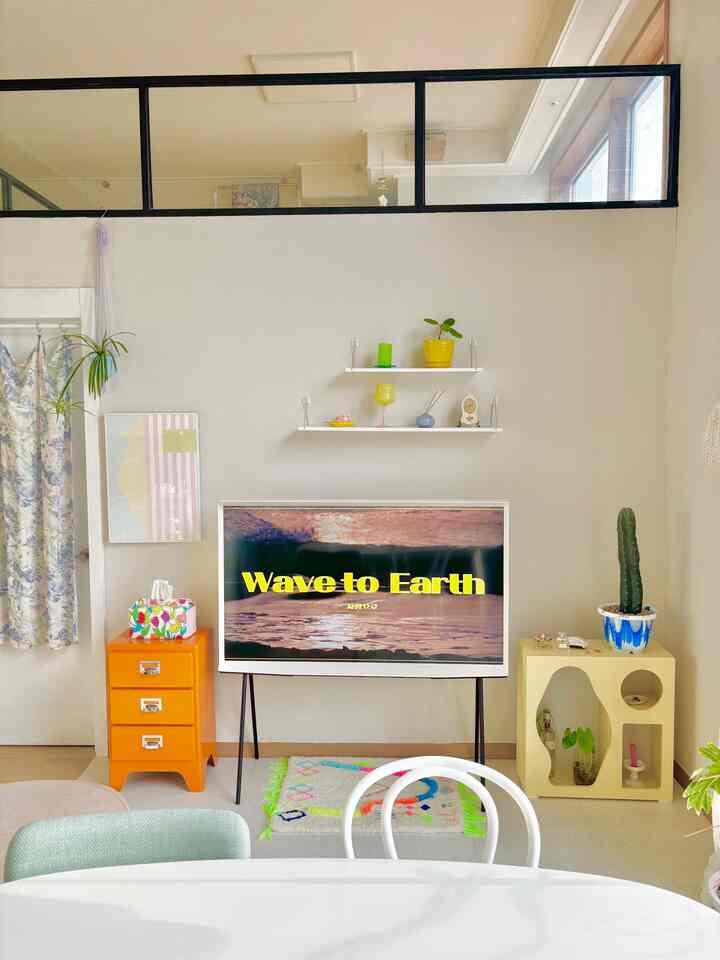 Modern living room with dominant white and orange accents, featuring a TV, wall shelves, colorful carpet, and plants creating a cozy atmosphere