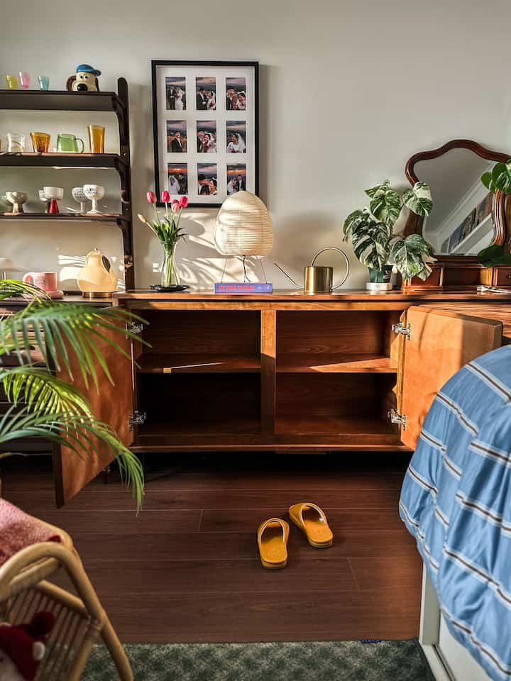 温かみのある木目調の家具が配された寝室兼リビング、写真額縁と植物が調和した雰囲気のある空間