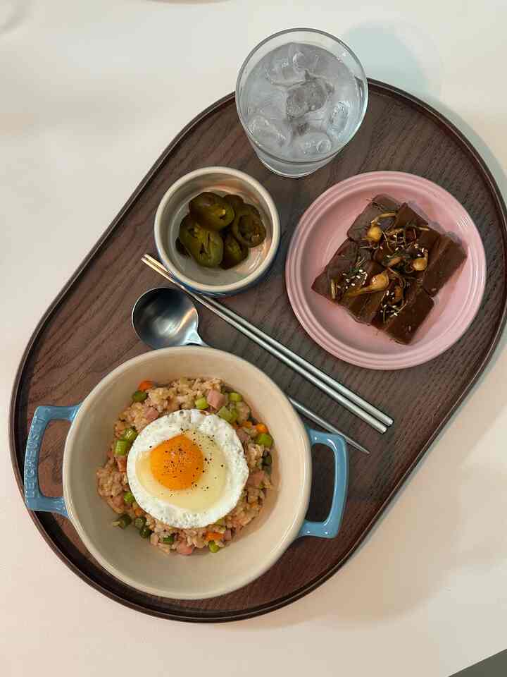 Wood tone dining surface featuring Le Creuset dishes and a wood tray with fried rice and side dishes in a cozy home cafe meal setup