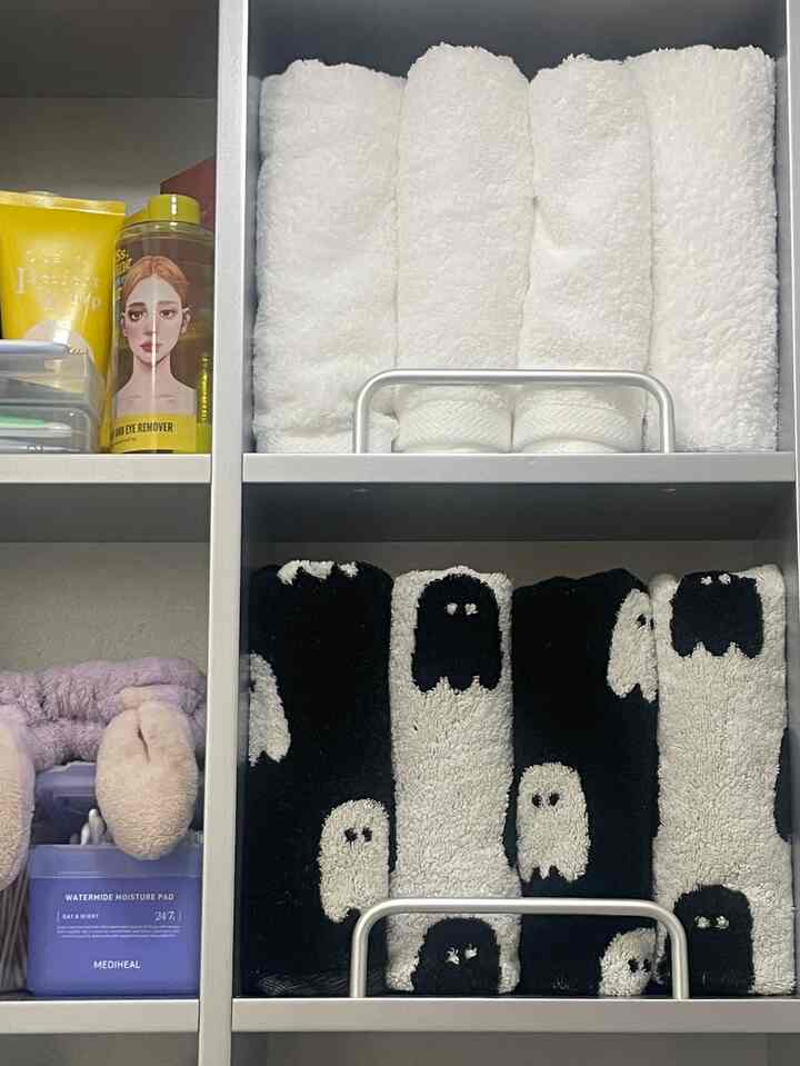 白と黒のタオルが整然と収納され、スキンケア製品が並ぶ清潔感のあるバスルーム収納スペース