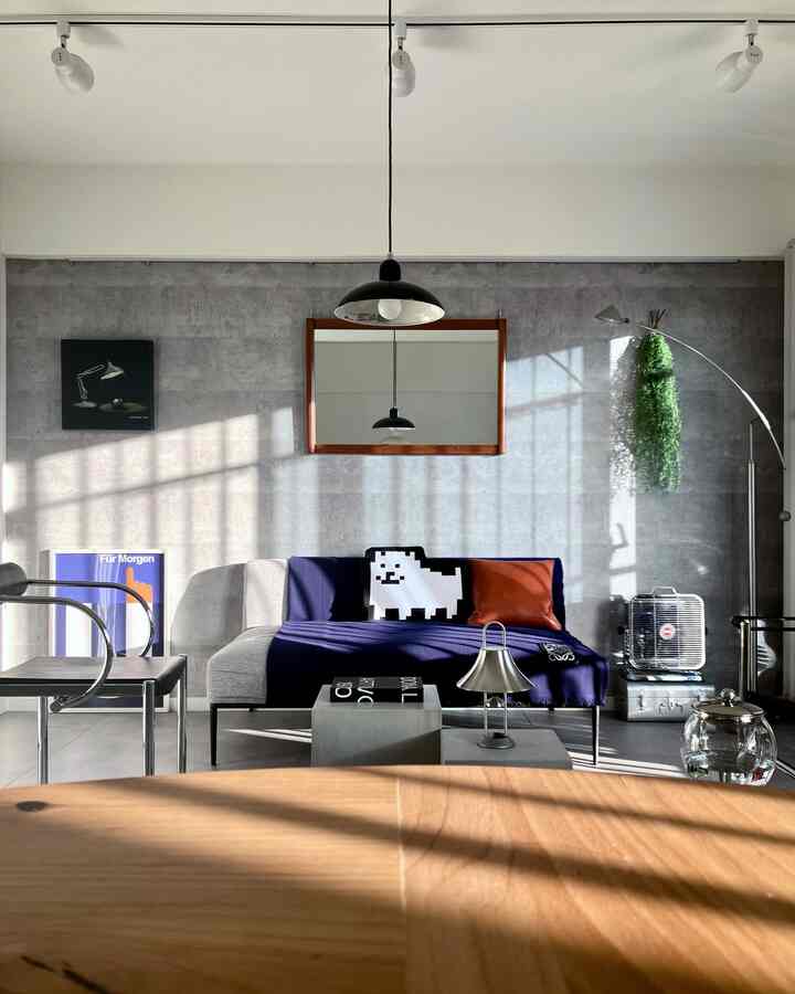 グレー調のインダストリアルなリビングルーム、中央にソファと青いクッション、木製テーブルが配置されたすっきりとした空間