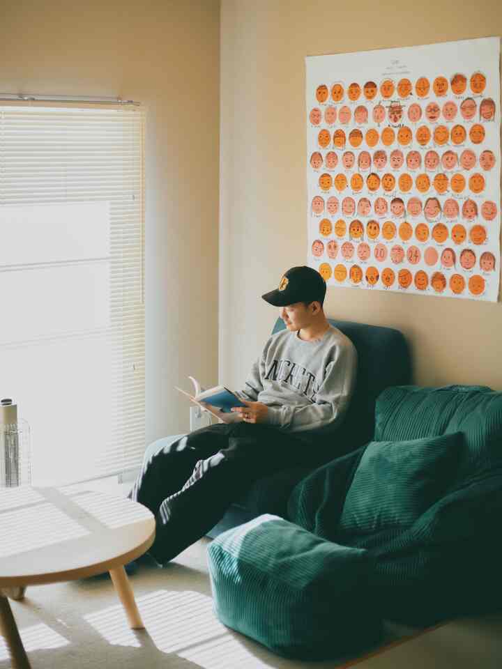 Warm beige and deep green toned living room featuring a sofa by the window and round wooden coffee table with cozy reading atmosphere