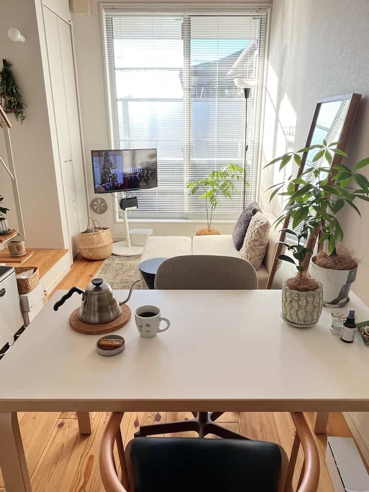 白と木目調の明るいワンルームリビング、ダイニングテーブルにコーヒーセットと観葉植物が配置された雰囲気あるおうちカフェ