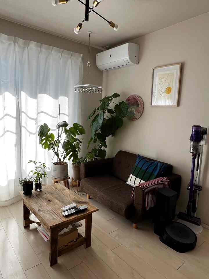 ベージュの壁と明るい木目の床を持つリビング、濃いブラウンのソファと木製ローテーブル、緑の観葉植物が配置されたナチュラルな雰囲気のインテリア