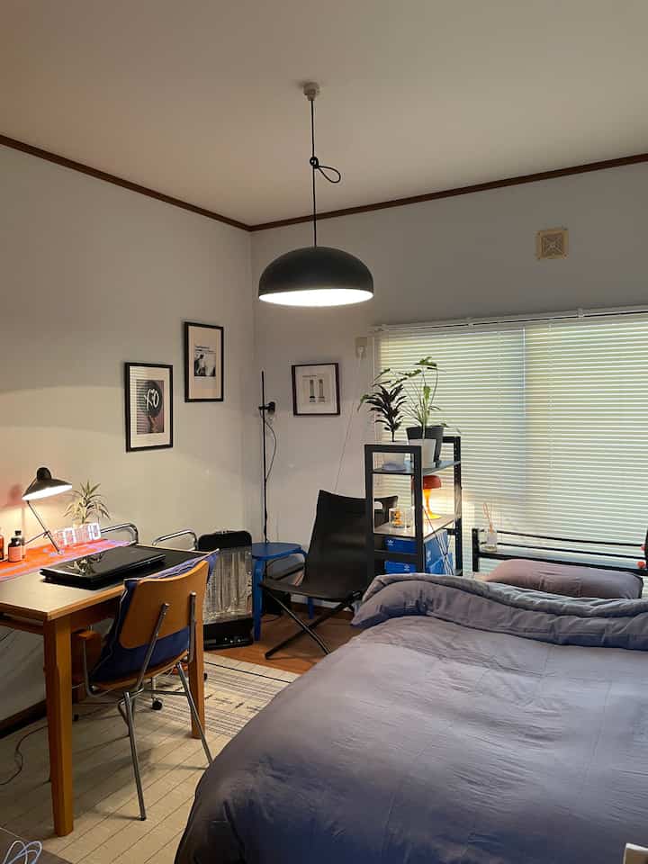 Natural-toned bedroom featuring a large bed, desk, and blinds, creating a cozy and functional studio apartment space