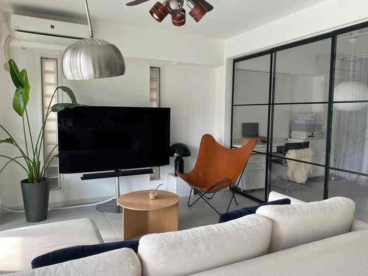 White and brown toned living room featuring mid-century modern furniture, large sofa, and plant in a hotel-like space